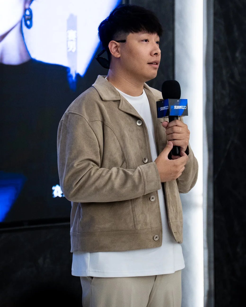 Jay 穿米色外套站在舞台上，拿著麥克風分享